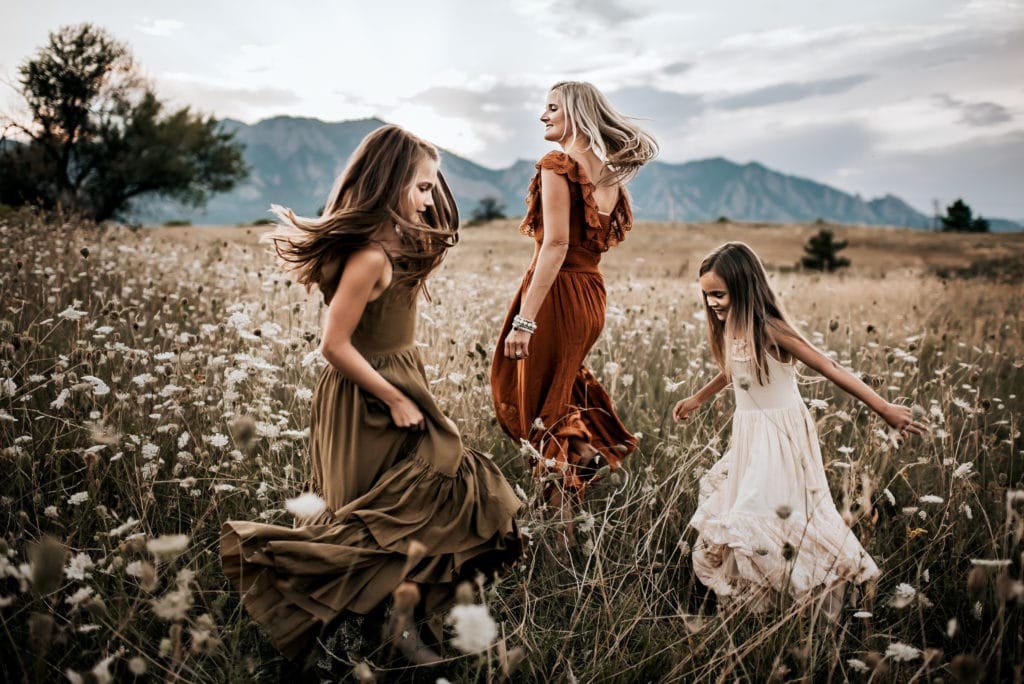 Online Family Photographer Education, a mother and her two daughters playfully dance in a meadow of wildflowers